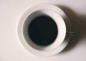 Clean minimalist shot of a black coffee cup on a white table, creating a serene ambiance.